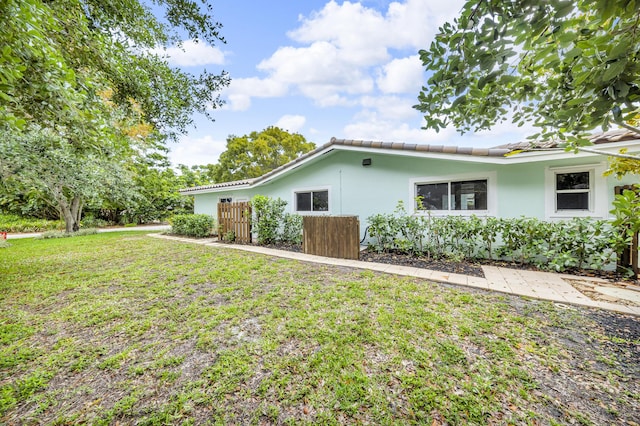 view of side of home with a lawn, stucco siding, a tiled roof, and fence