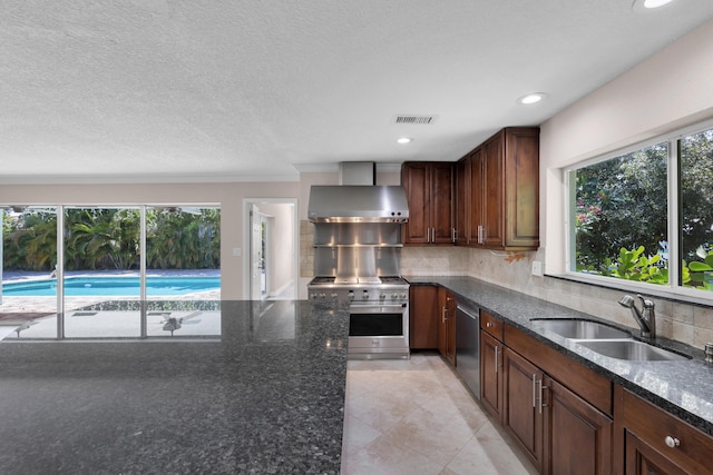 kitchen featuring wall chimney range hood, stainless steel appliances, a healthy amount of sunlight, and a sink