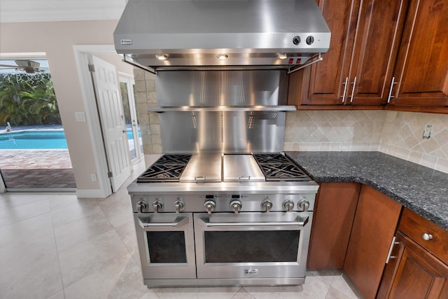 kitchen with dark stone counters, wall chimney exhaust hood, decorative backsplash, and light tile patterned floors