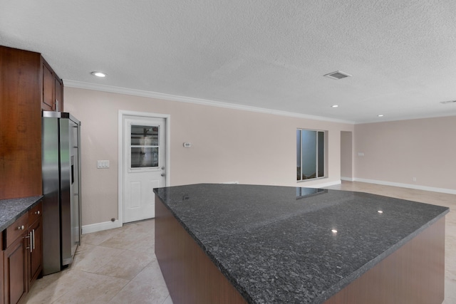 kitchen with freestanding refrigerator, a textured ceiling, baseboards, ornamental molding, and a spacious island