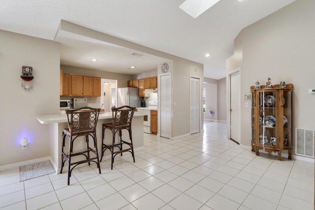 kitchen with under cabinet range hood, light countertops, visible vents, white appliances, and a peninsula