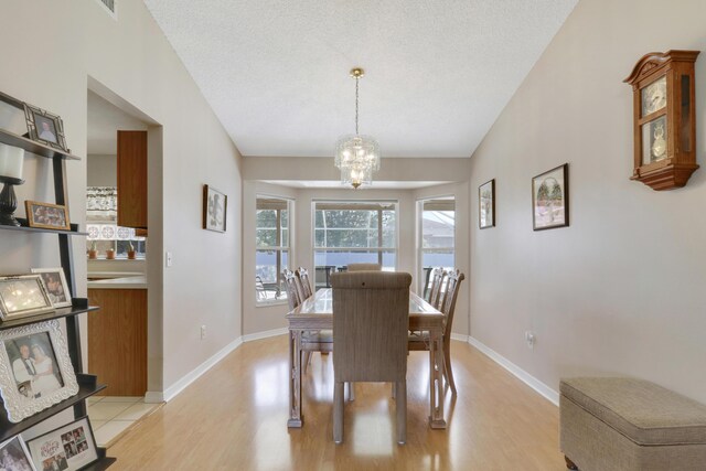 dining space with lofted ceiling, light wood finished floors, baseboards, and a notable chandelier