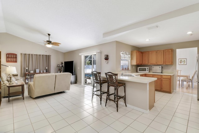 kitchen with light countertops, a breakfast bar, white microwave, a peninsula, and open floor plan