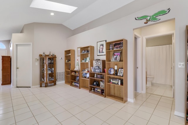 hallway featuring baseboards, a skylight, high vaulted ceiling, and light tile patterned floors