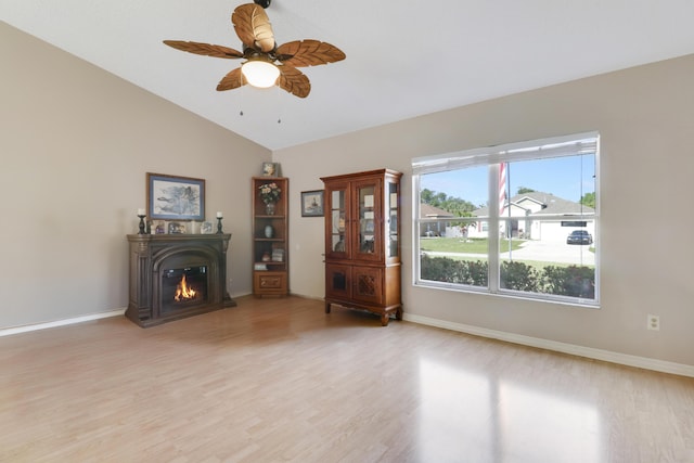 living room with vaulted ceiling, a ceiling fan, light wood-style floors, baseboards, and a glass covered fireplace