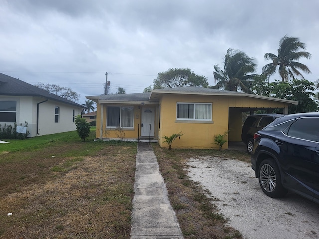 view of front facade featuring an attached carport, driveway, stucco siding, and a front lawn