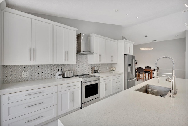 kitchen featuring vaulted ceiling, white cabinetry, wall chimney exhaust hood, stainless steel appliances, and a sink