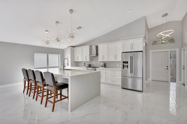 kitchen featuring an inviting chandelier, wall chimney range hood, visible vents, appliances with stainless steel finishes, and a sink