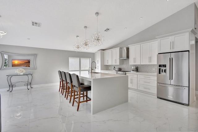 kitchen with visible vents, wall chimney exhaust hood, a sink, appliances with stainless steel finishes, and marble finish floor