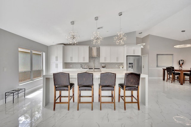 kitchen featuring wall chimney exhaust hood, high quality fridge, a chandelier, a large island with sink, and marble finish floor