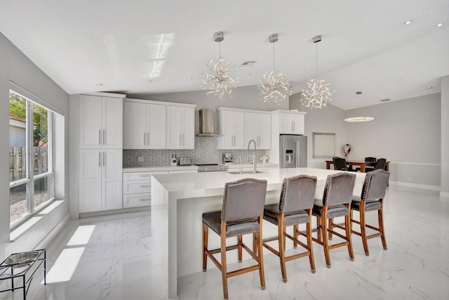 kitchen featuring wall chimney exhaust hood, vaulted ceiling, a large island, marble finish floor, and high end fridge