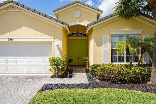 9961 SW Glenbrook Dr, Port Saint Lucie, FL 34987 - view of exterior entry with a tile roof, decorative driveway, stucco siding, and an attached garage