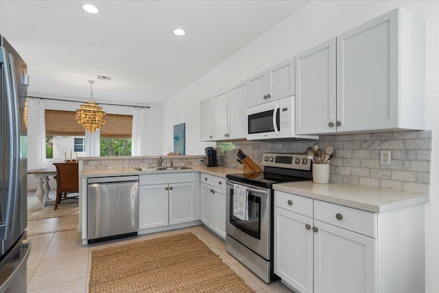 9961 SW Glenbrook Dr, Port Saint Lucie, FL 34987 - kitchen with decorative backsplash, a peninsula, stainless steel appliances, a sink, and a notable chandelier