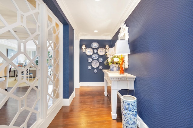 hall with wallpapered walls, wood-type flooring, ornamental molding, and baseboards