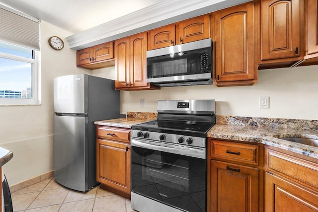 kitchen featuring brown cabinets, light stone countertops, stainless steel appliances, and light tile patterned floors