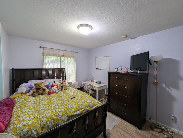 bedroom with baseboards, a textured ceiling, and light wood finished floors