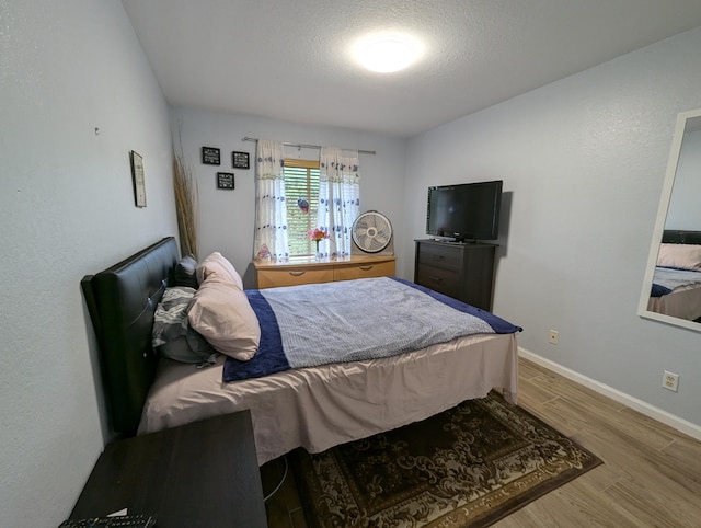 bedroom with baseboards, wood finished floors, and a textured ceiling