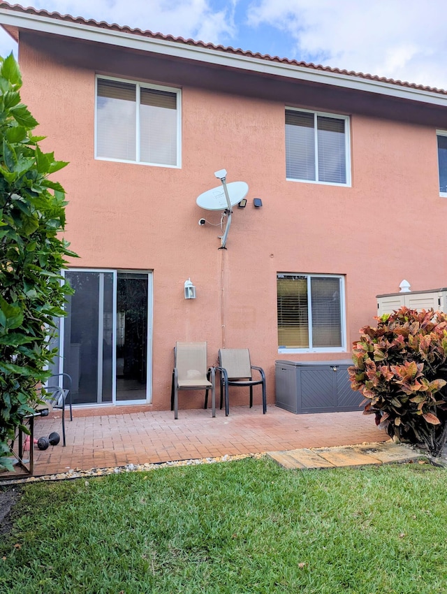back of house with stucco siding, a patio area, and a yard