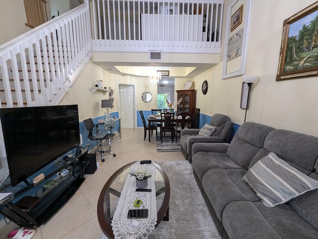 living area featuring stairs, light tile patterned floors, baseboards, visible vents, and a towering ceiling