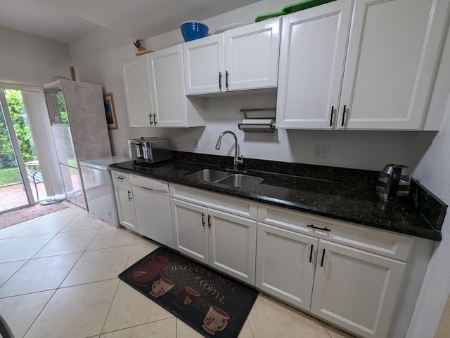 kitchen featuring light tile patterned flooring, dark stone counters, white cabinetry, a sink, and white dishwasher