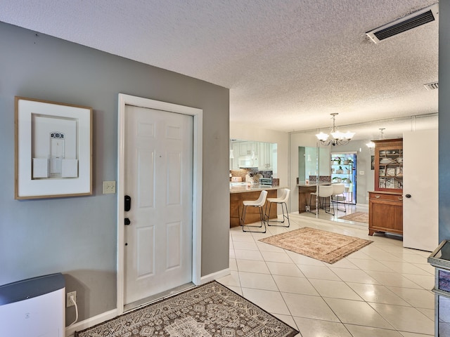 entryway featuring a textured ceiling, an inviting chandelier, visible vents, and light tile patterned floors