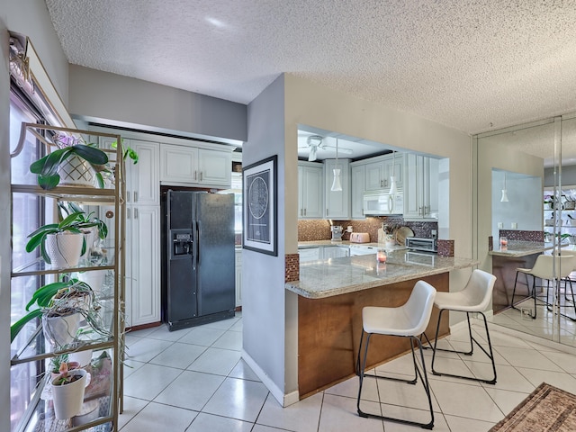 kitchen with white microwave, light tile patterned floors, a textured ceiling, white cabinetry, and black fridge