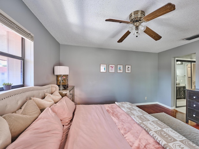 bedroom featuring baseboards, a textured ceiling, connected bathroom, visible vents, and wood finished floors