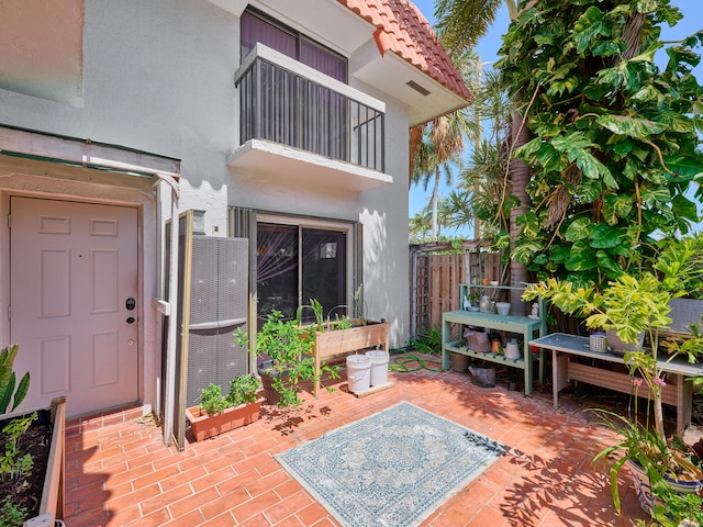 view of exterior entry featuring a patio, a balcony, stucco siding, a tiled roof, and fence