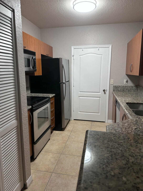 162 SW Peacock Blvd Unit 205, Port Saint Lucie, FL 34986 - kitchen with stainless steel appliances, a textured ceiling, light tile patterned floors, a sink, and brown cabinets