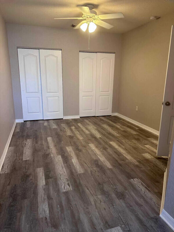 162 SW Peacock Blvd Unit 205, Port Saint Lucie, FL 34986 - unfurnished bedroom with multiple closets, dark wood-style floors, baseboards, and a ceiling fan