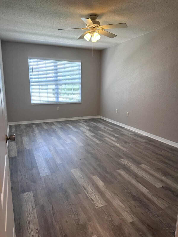162 SW Peacock Blvd Unit 205, Port Saint Lucie, FL 34986 - empty room featuring dark wood-type flooring, a textured ceiling, a ceiling fan, and baseboards