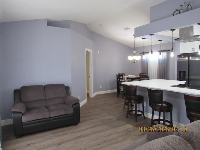 443 SW Homeland Rd, Port Saint Lucie, FL 34953 - kitchen with stainless steel fridge, a breakfast bar area, vaulted ceiling, light wood finished floors, and white cabinets
