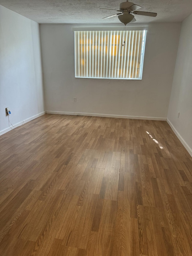 spare room with baseboards, a ceiling fan, wood finished floors, and a textured ceiling