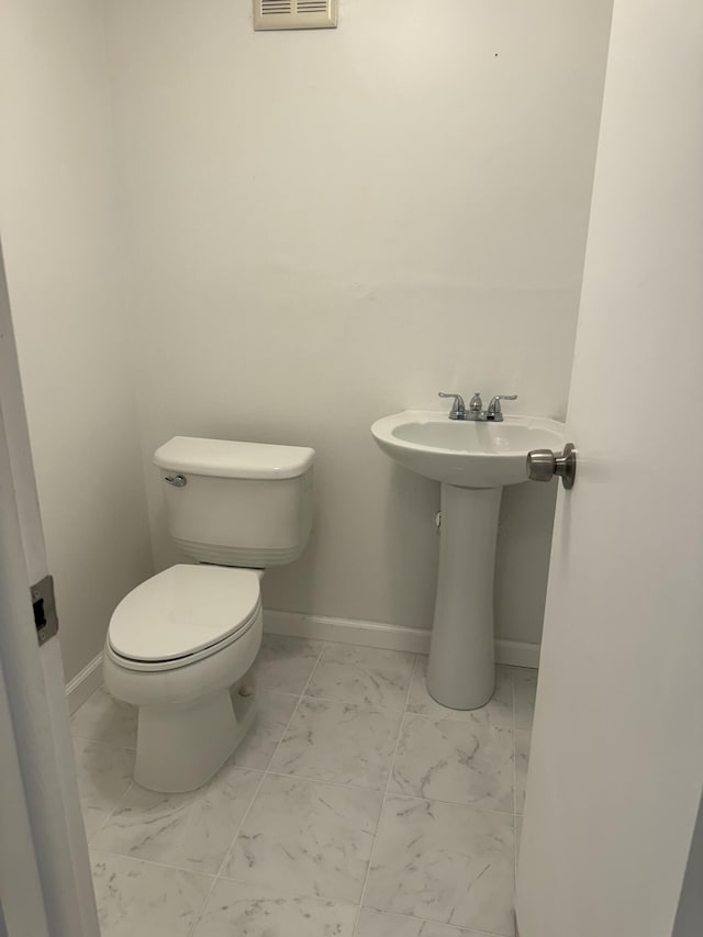 half bathroom with marble finish floor, toilet, and baseboards