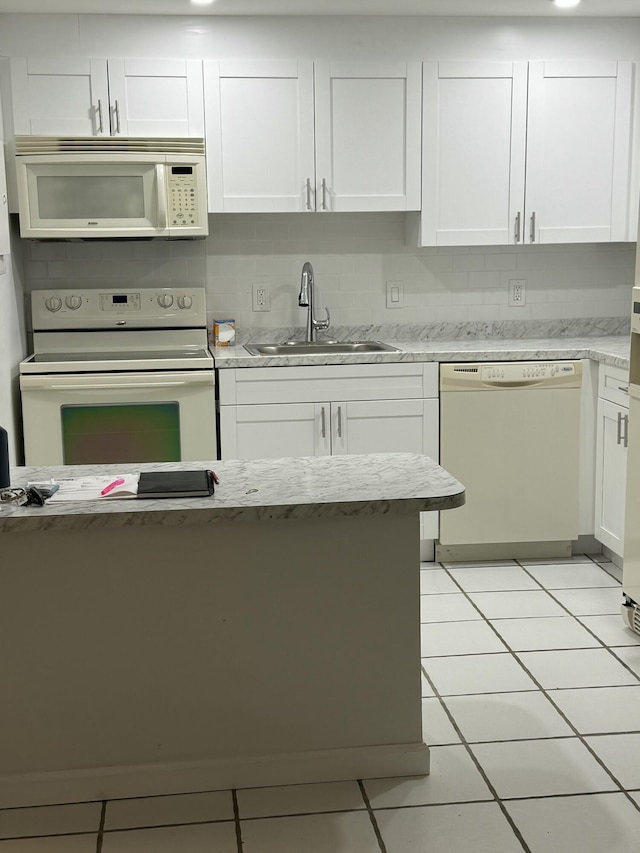 kitchen featuring a sink, light tile patterned flooring, white cabinetry, white appliances, and light stone countertops