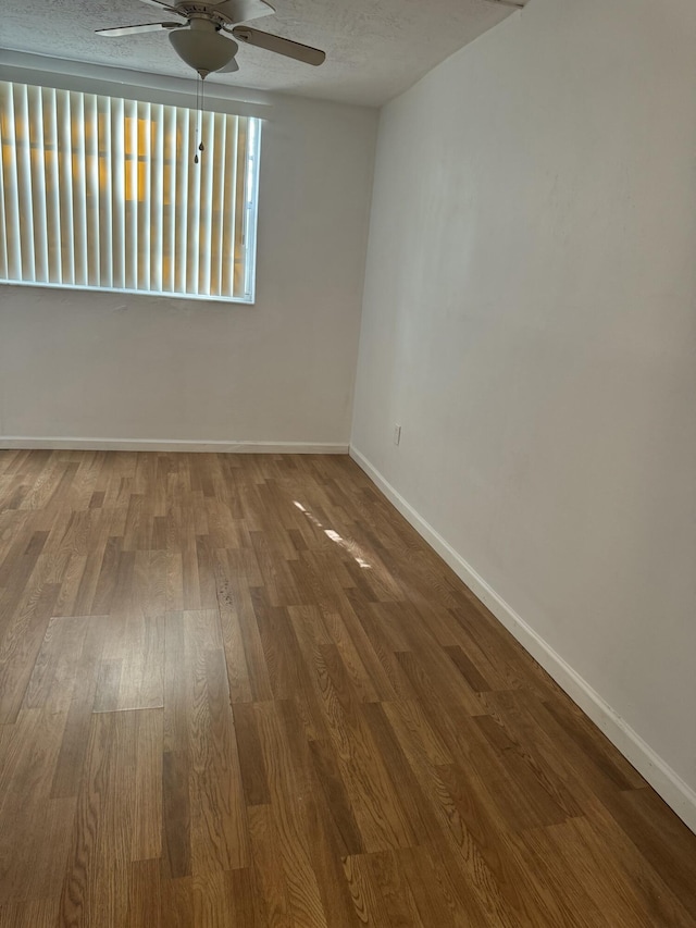 spare room with wood finished floors, a ceiling fan, and baseboards