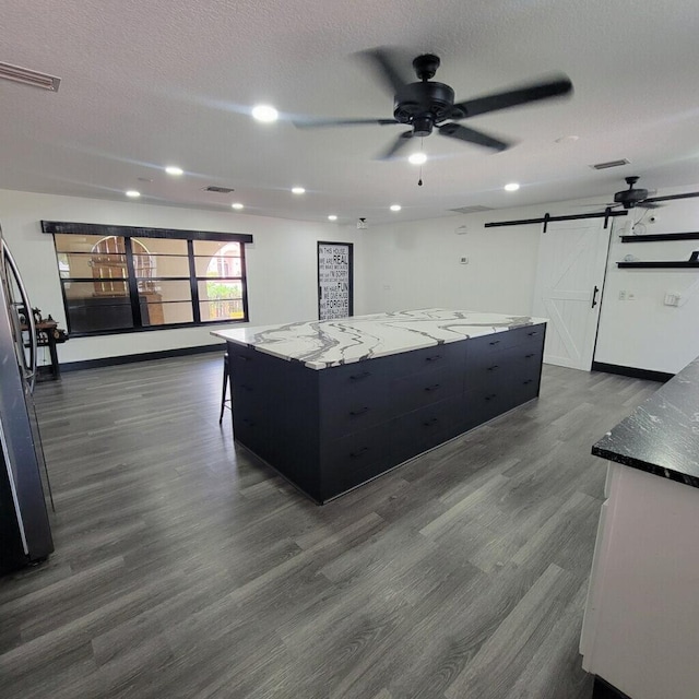 2379 Carambola Rd, West Palm Beach, FL 33406 - kitchen with a barn door, ceiling fan, a large island, dark cabinetry, and dark wood-style flooring