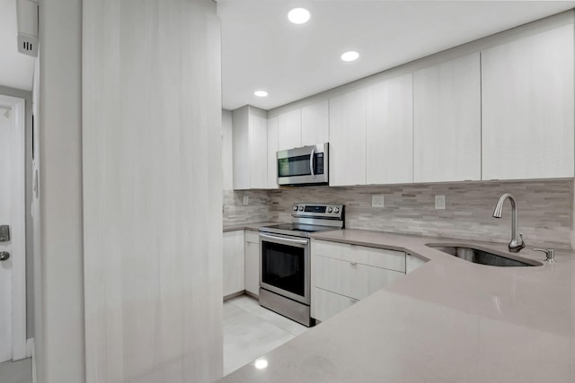 kitchen featuring decorative backsplash, white cabinets, a sink, and appliances with stainless steel finishes