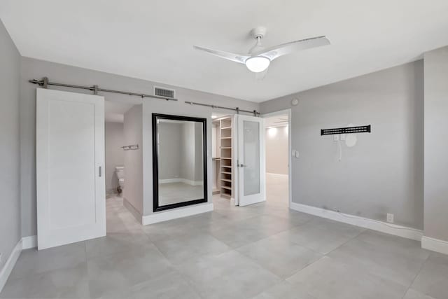 unfurnished bedroom with baseboards, a barn door, visible vents, and a spacious closet