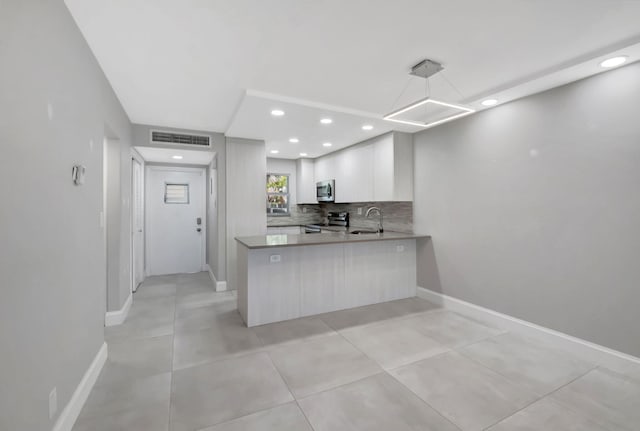 kitchen with a sink, tasteful backsplash, a peninsula, stainless steel appliances, and visible vents