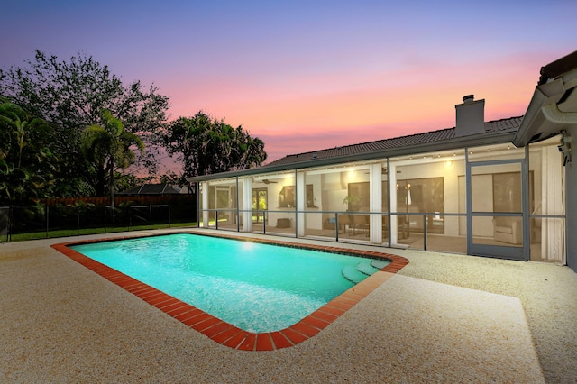 pool at dusk featuring fence, a patio area, a fenced in pool, and a sunroom