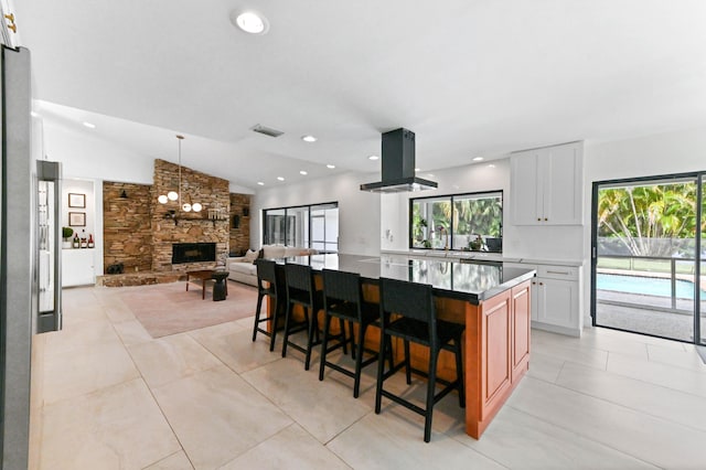 kitchen with vaulted ceiling, a kitchen breakfast bar, island range hood, a fireplace, and a kitchen island