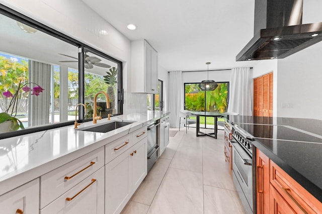 kitchen with white cabinetry, wall chimney range hood, a sink, stainless steel range, and ceiling fan