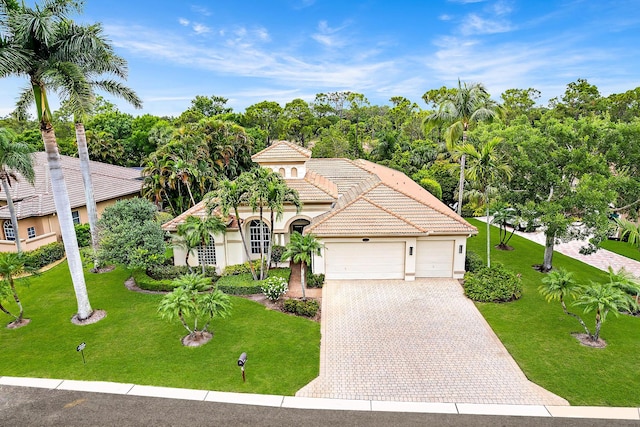 mediterranean / spanish home featuring a tiled roof, stucco siding, a front lawn, an attached garage, and driveway