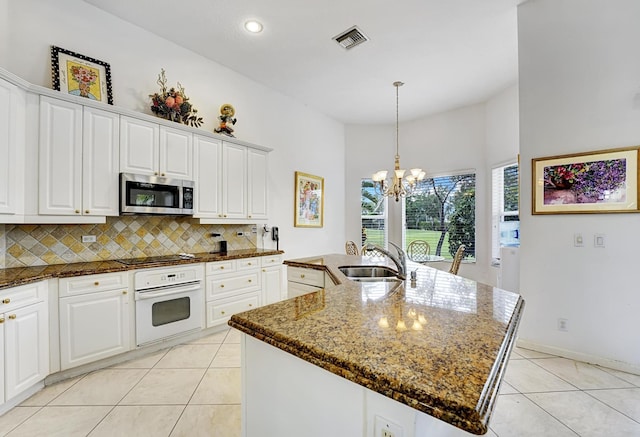 kitchen with white oven, stainless steel microwave, a sink, light tile patterned floors, and a chandelier