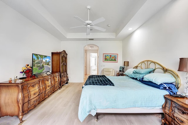 bedroom featuring arched walkways, a tray ceiling, light wood-type flooring, recessed lighting, and a ceiling fan