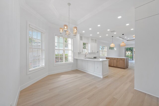 17065 Bay St, Jupiter, FL 33477 - kitchen with crown molding, light wood-style floors, glass insert cabinets, a peninsula, and light countertops