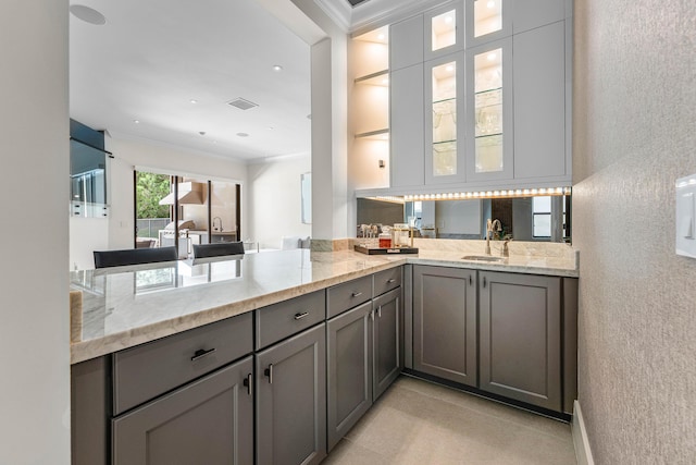 16491 Gateway Bridge Dr, Delray Beach, FL 33446 - kitchen featuring gray cabinets, a sink, ornamental molding, light stone countertops, and glass insert cabinets