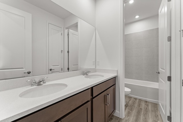 bathroom with double vanity, wood finished floors, toilet, and a sink