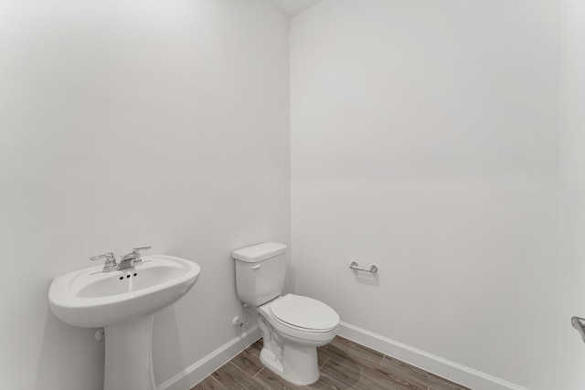half bathroom with baseboards, wood finished floors, and toilet